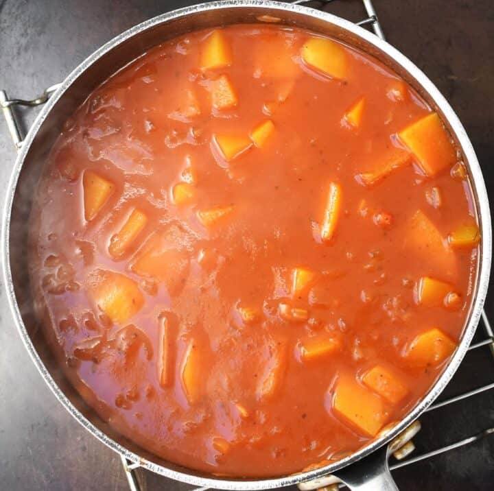 Soup with chunks of butternut squash and tomato in pot.