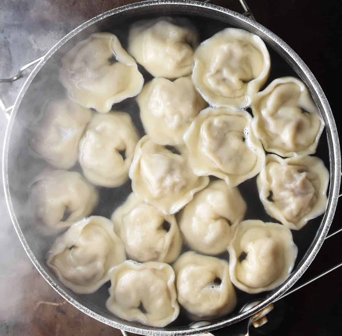 Top down view of boiling kolduny dumplings in pot of water.