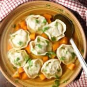 Top down view of koldunai in broth in brown bowl with spoon.