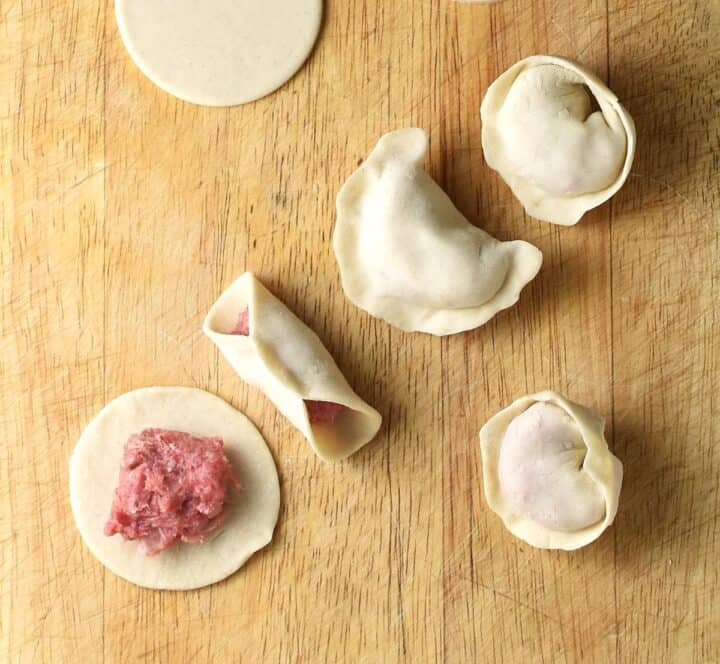 Forming koldunai dumplings on top of wooden surface.