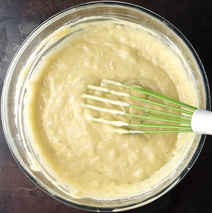 Top down view of plum cake batter in glass bowl with green whisk.