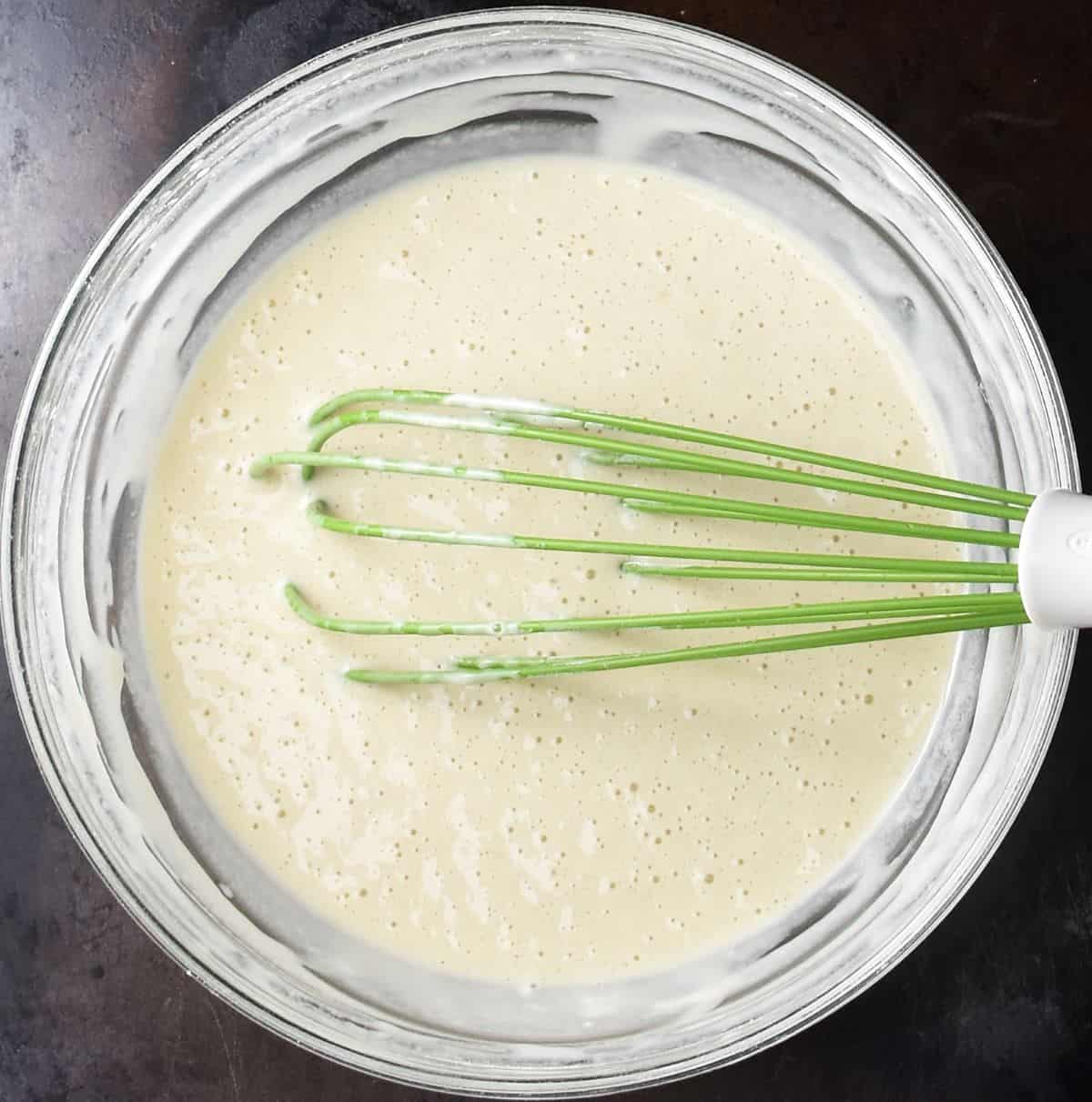 Top down view of smooth batter for sauerkraut pancakes in glass bowl with whisk.