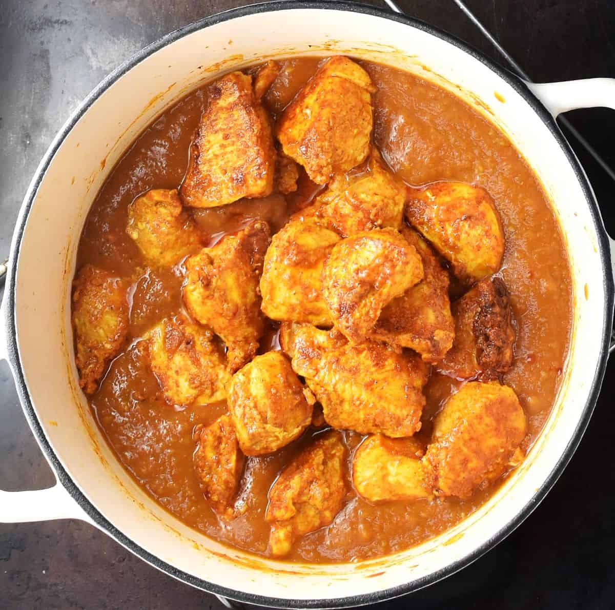 Assembling chicken and pumpkin curry in white pot.