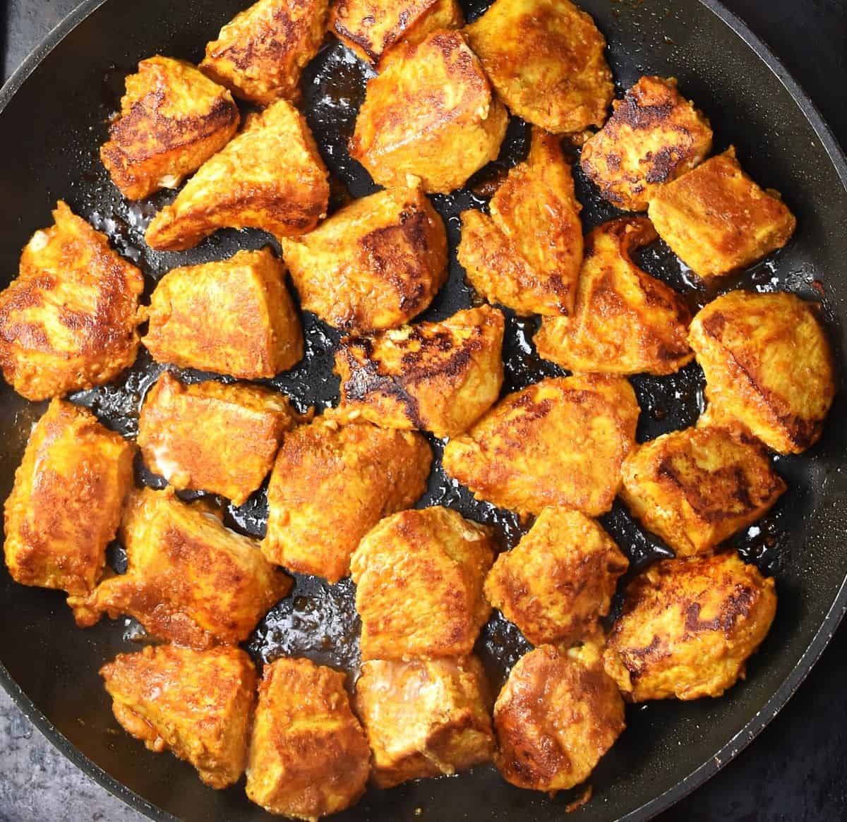 Seared spiced chunks of chicken in large pan.