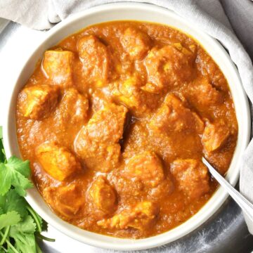 Top down view of chicken pumpkin curry in grey bowl with spoon.