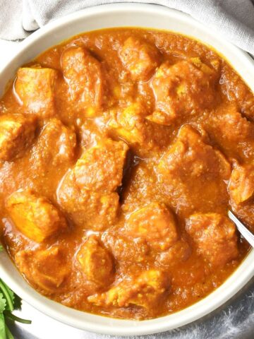 Top down view of chicken pumpkin curry in grey bowl with spoon.