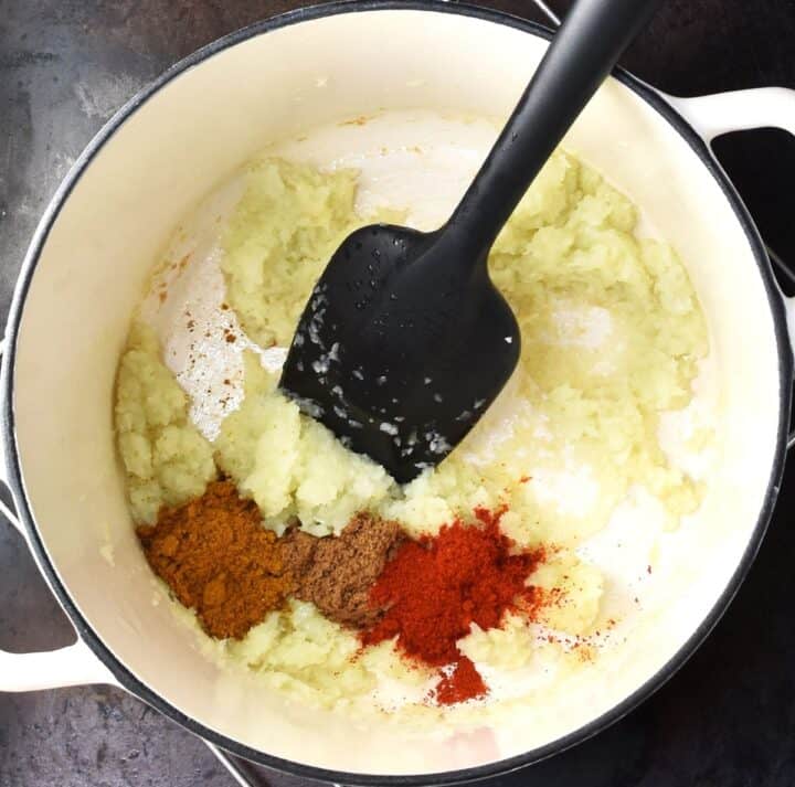Pureed onion with spices and black spoon in white pot.