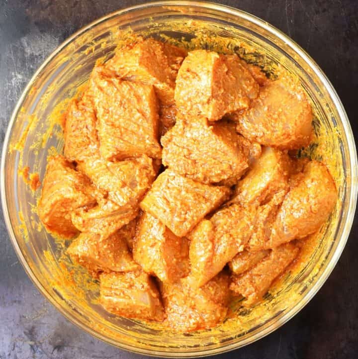 Top down view of chicken pieces coated in spices in glass bowl.