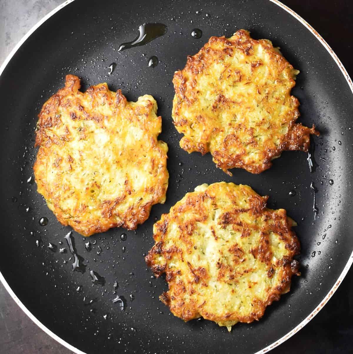 Top down view of 3 sauerkraut pancakes in pan.