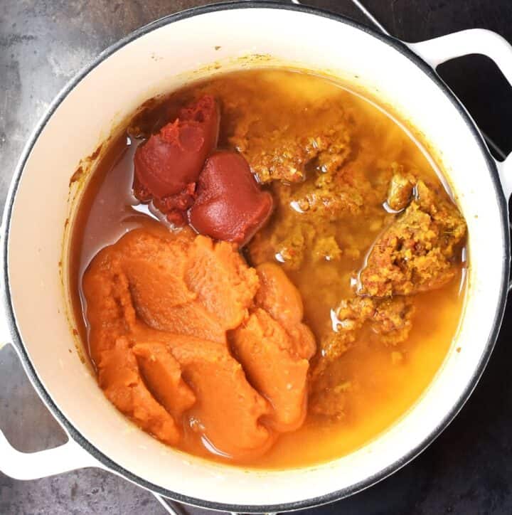Pumpkin puree, tomato puree, spices and water in white pot.