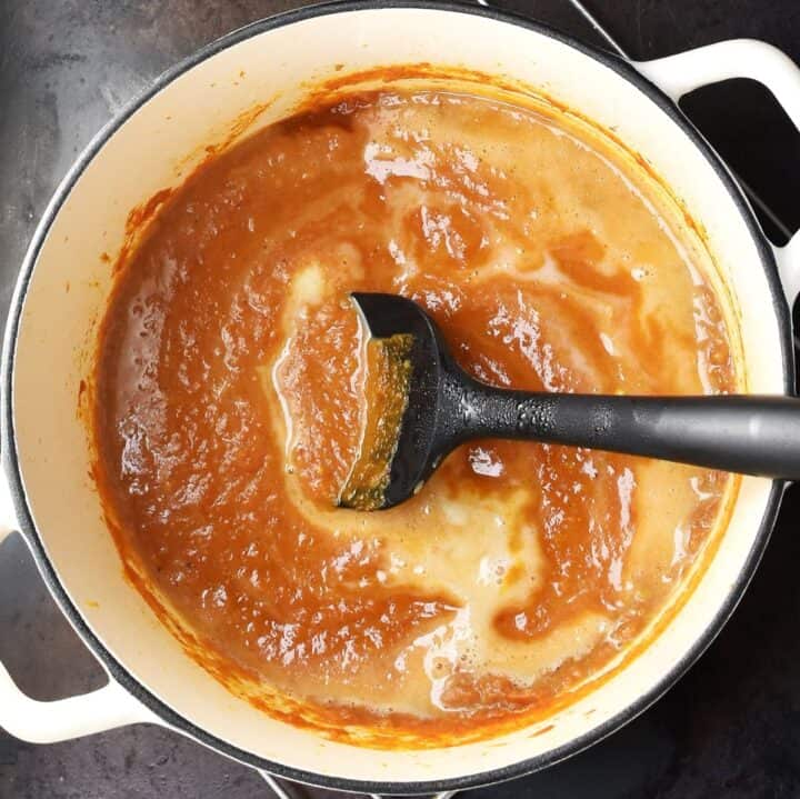 Top down view of creamy pumpkin curry sauce with black spoon in white pot.