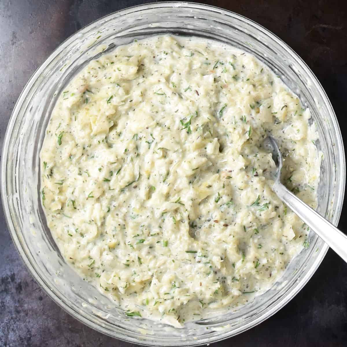 Top down view of sauerkraut pancake batter in glass bowl with spoon.