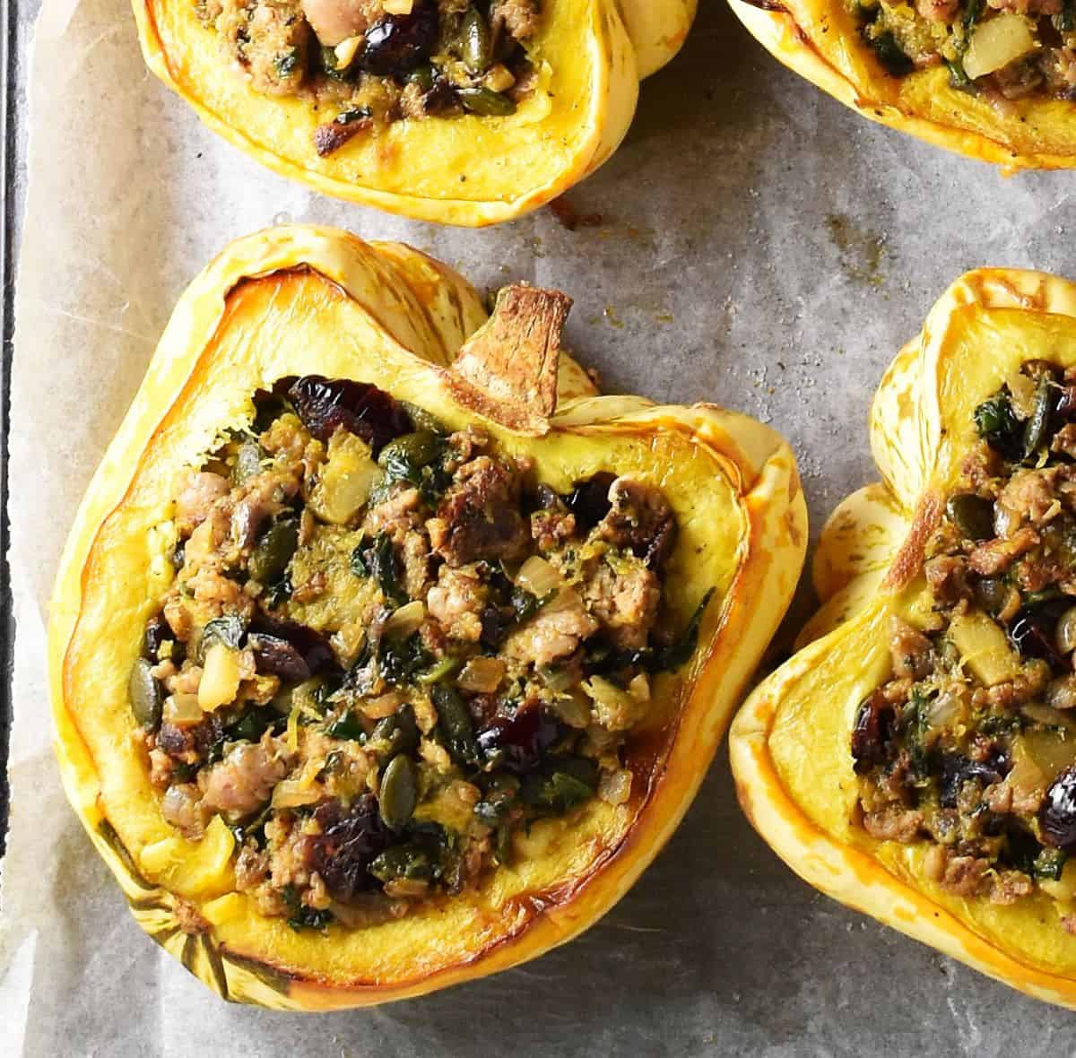 Top down view of acorn squash stuffed with sausage mixture on top of parchment.