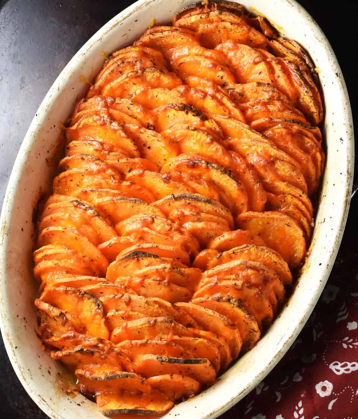 Top down view of roasted scalloped sweet potatoes with browned crispy top in white ceramic dish.