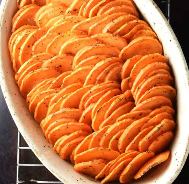 Baked scalloped sweet potatoes arranged vertically in oval dish.