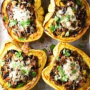 Top down view of 4 sausage stuffed acorn squash with herbs and cheese on top.