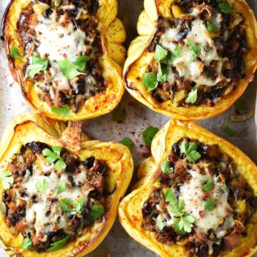 Top down view of 4 sausage stuffed acorn squash with herbs and cheese on top.