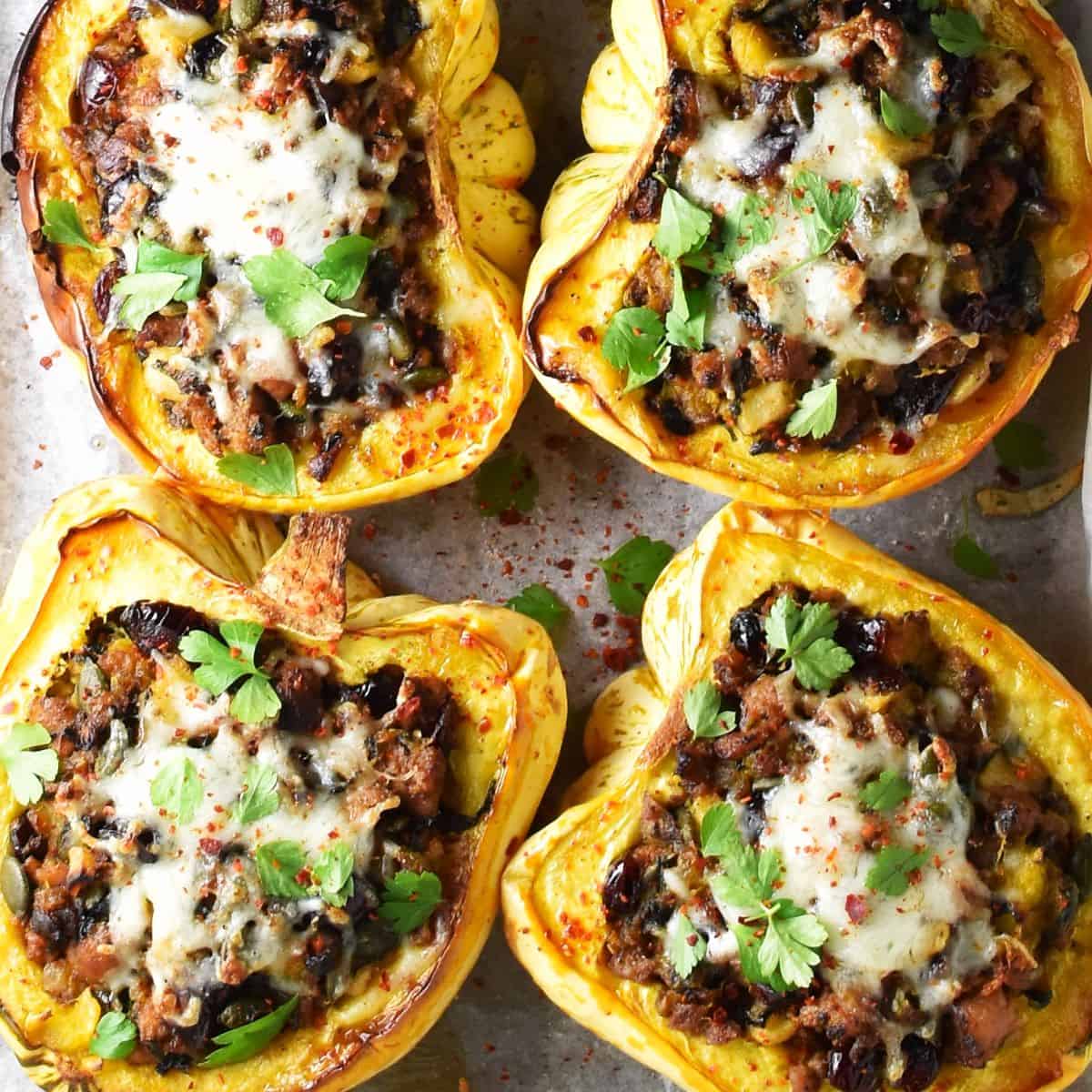 Top down view of 4 sausage stuffed acorn squash with herbs and cheese on top.