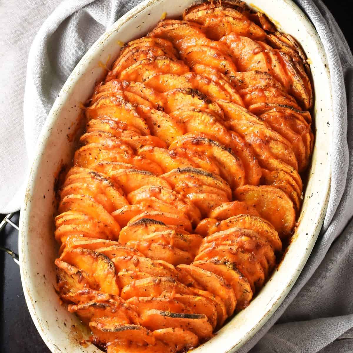 Top down view of scalloped sweet potatoes in white oval dish.