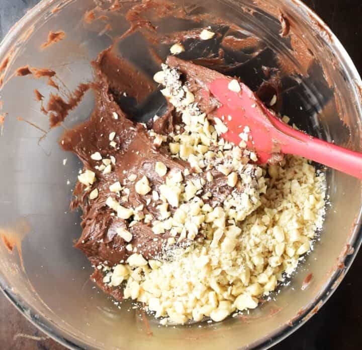 Frosting mixture with chopped hazelnuts in glass bowl with red spatula.
