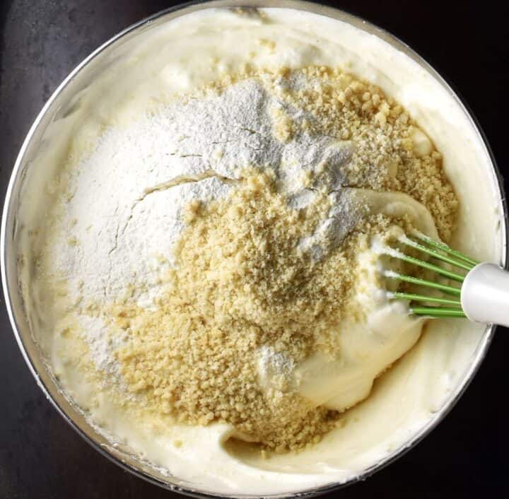 Fluffy torte batter with flour and hazelnuts in bowl with whisk.