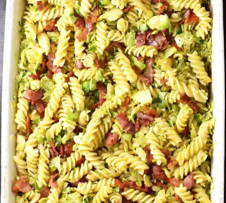 Top down view of assembled pasta with brussels sprouts and bacon in rectangular dish.
