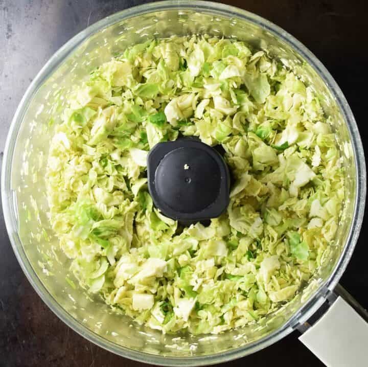 Shredded brussels sprouts in food processor bowl.