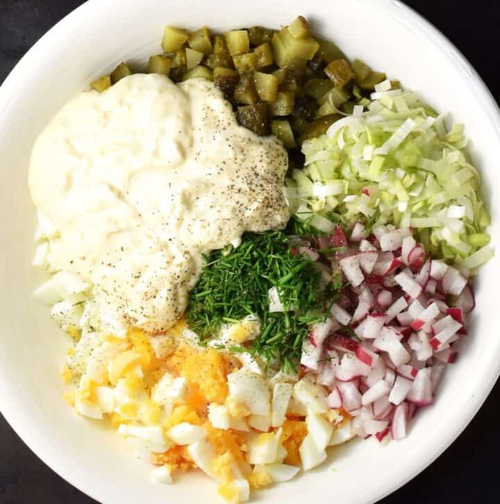 Top down view of egg and dill pickle salad components with creamy dressing in large shallow white bowl.