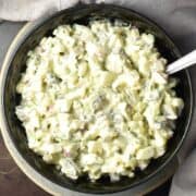 Top down view of creamy dill pickle egg salad in black bowl with spoon.