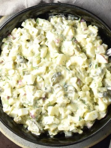 Top down view of creamy dill pickle egg salad in black bowl with spoon.