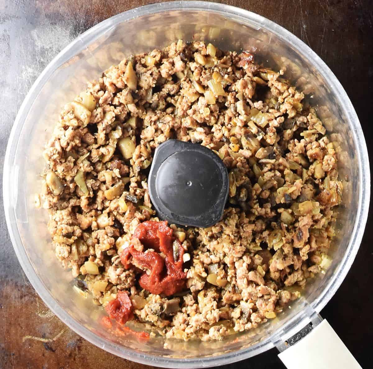 Top down view of ground meat with tomato paste in food processor.