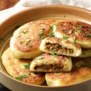 Side view of stuffed potato cakes in brown bowl.