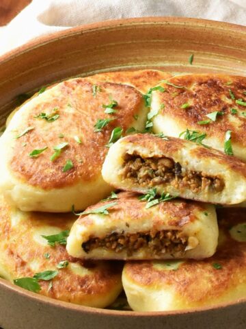 Side view of stuffed potato cakes in brown bowl.