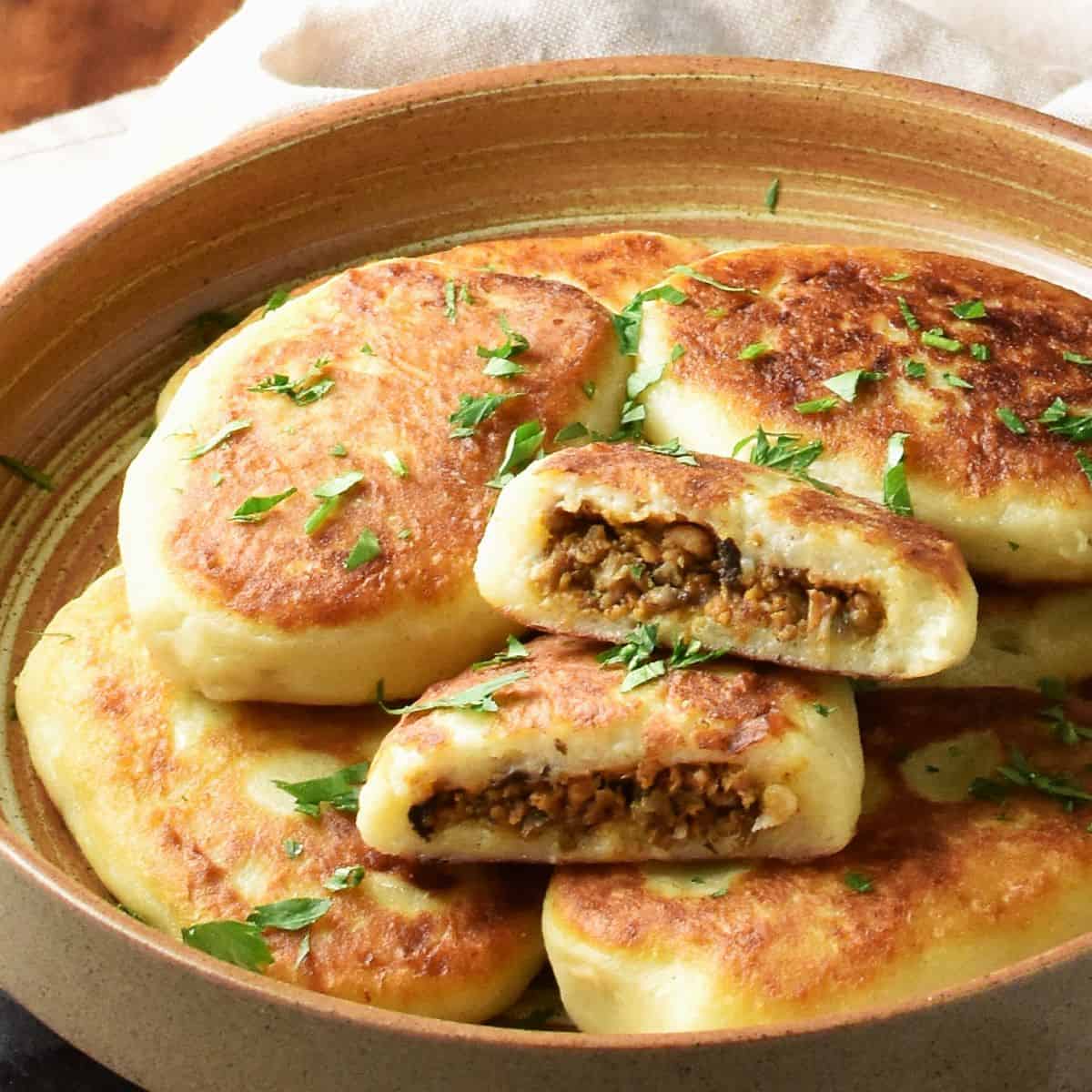 Side view of stuffed potato cakes in brown bowl.