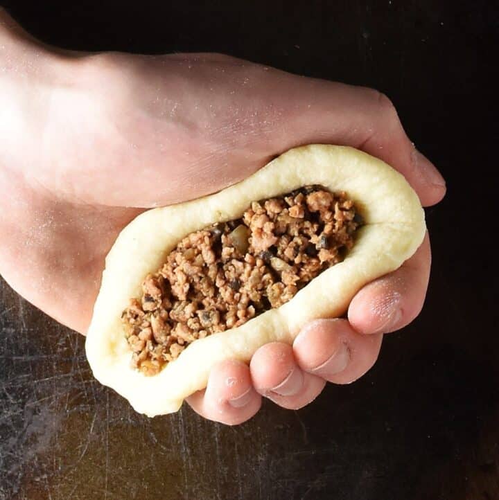 Hand holding meat stuffed potato cake.