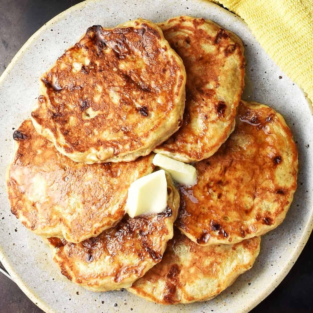 Top down view of cottage cheese banana pancakes with knob of butter on speckled plate.