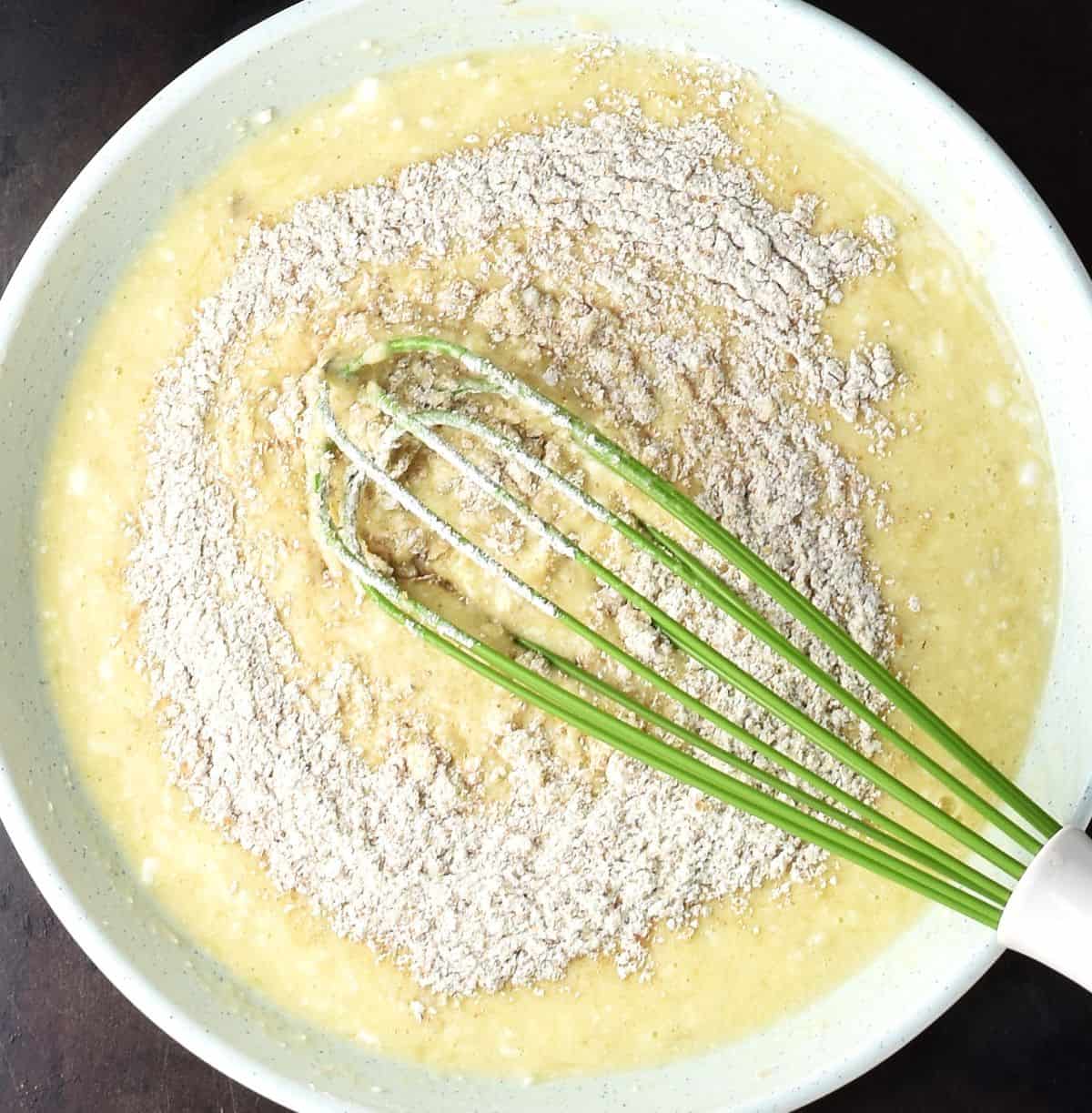 Pancake batter with flour visible and whisk in shallow bowl.
