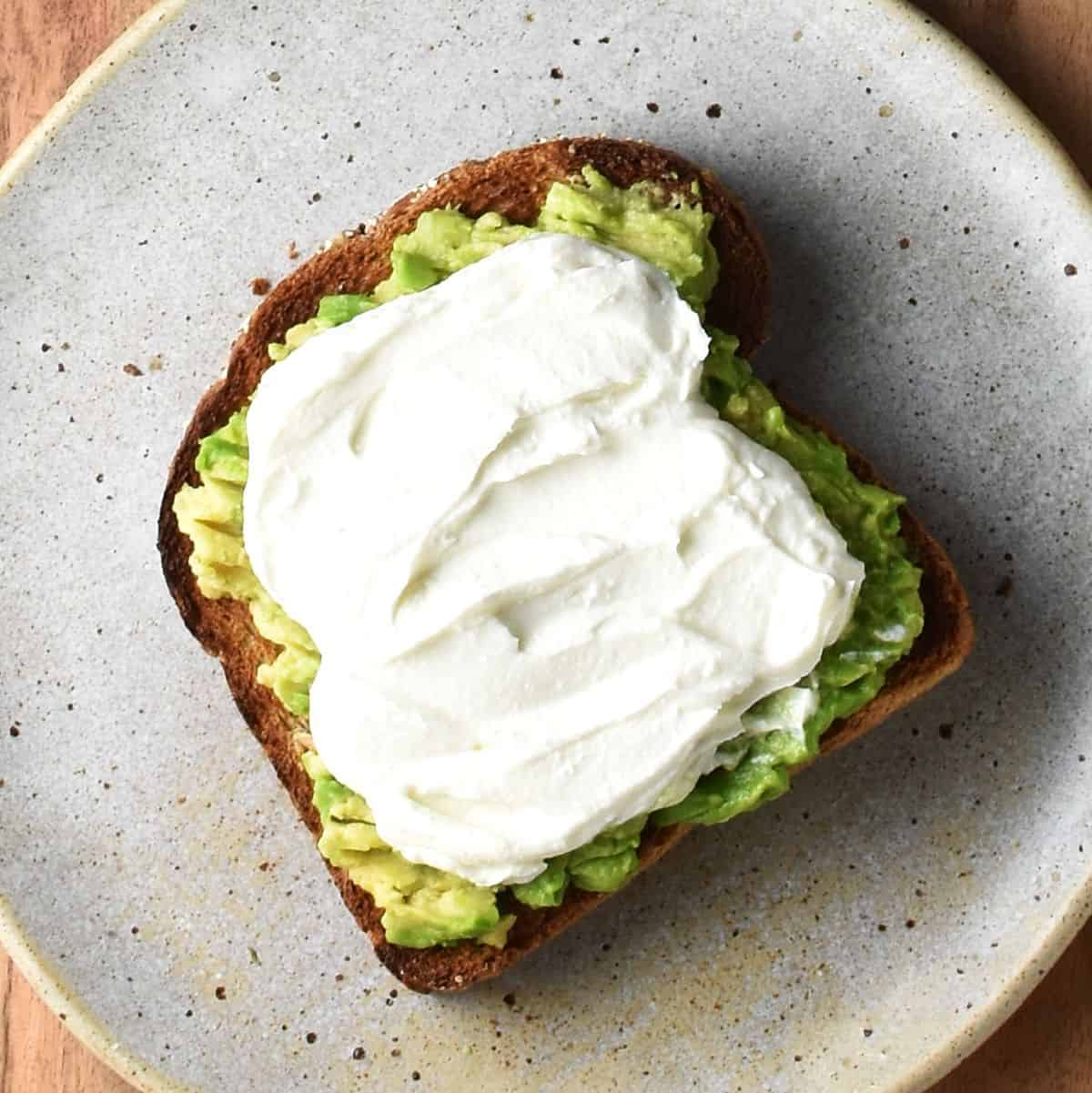 Toast with smashed avocado and creamy feta on speckled plate.