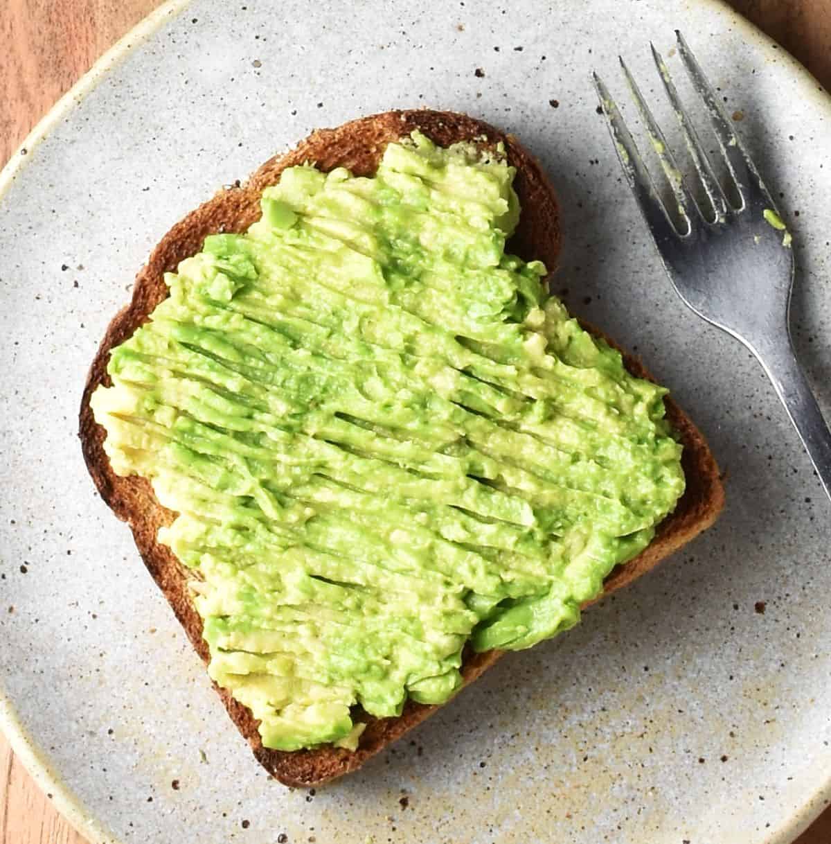 Top down view of toast with avocado on plate with fork.