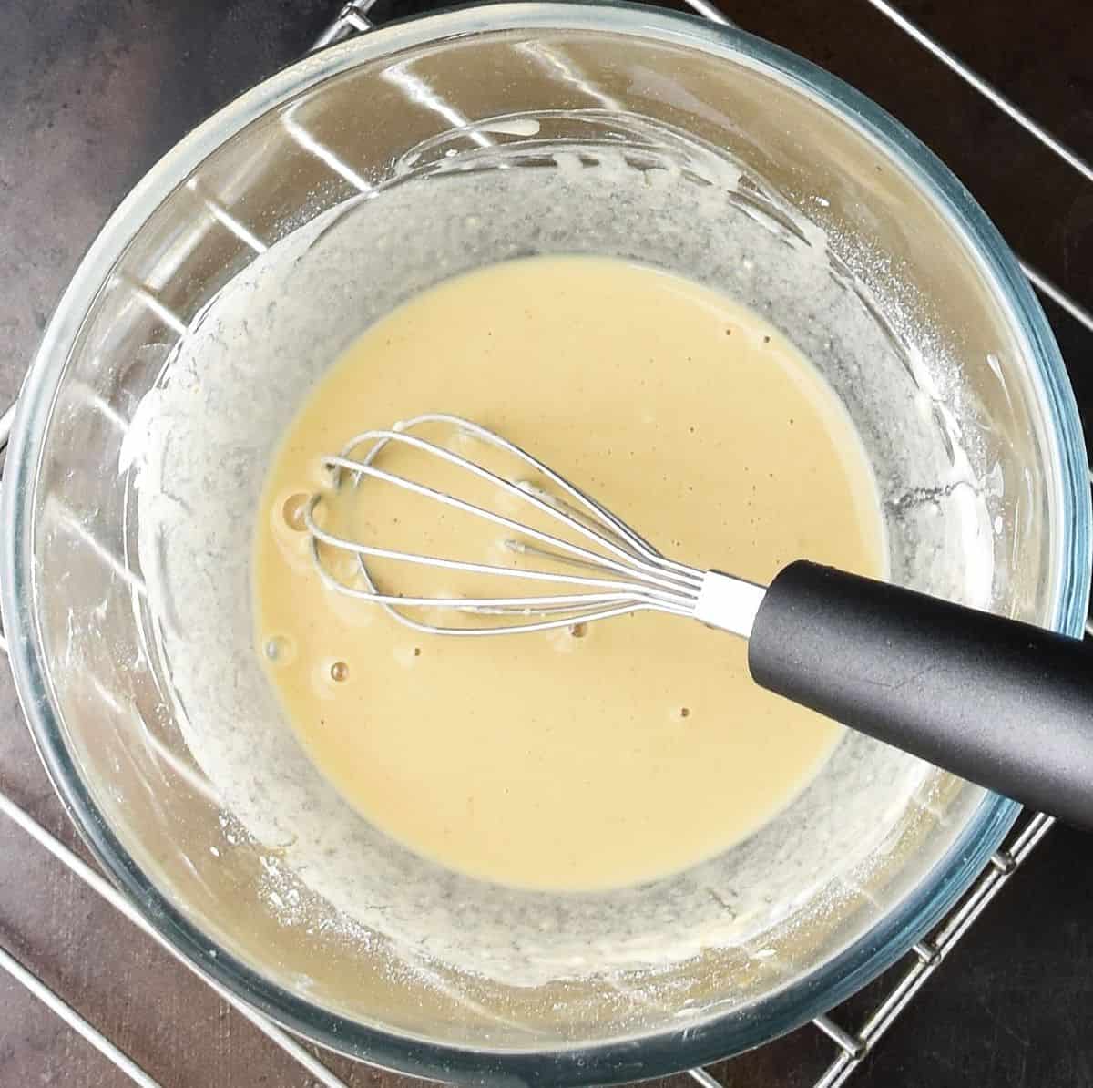 Thickening gravy mixture in glass bowl with whisk.