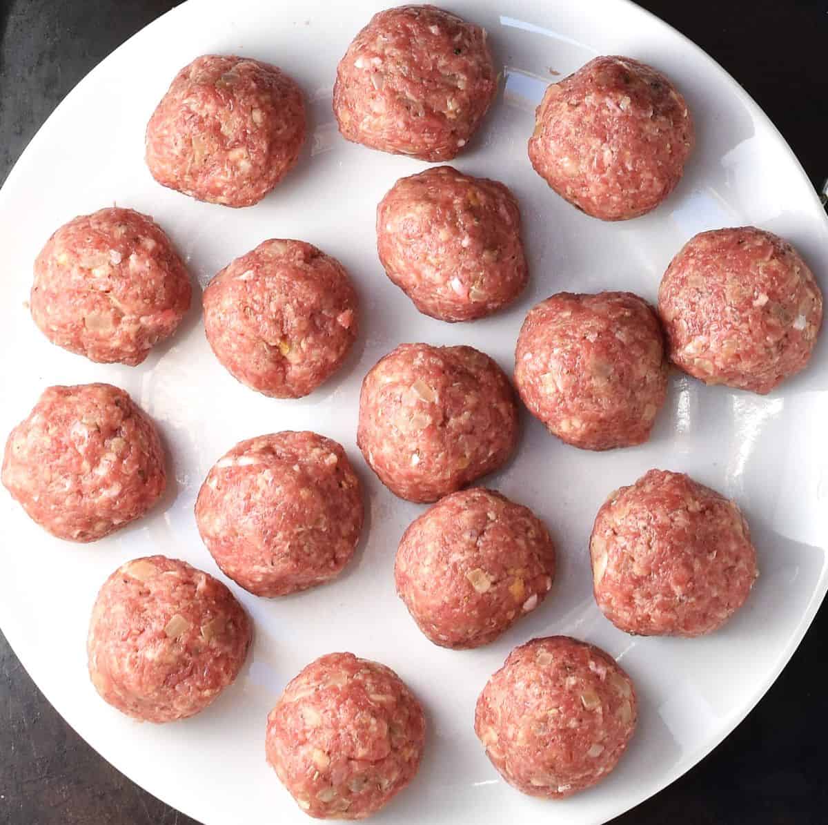 Raw turkey meatballs on top of white plate.