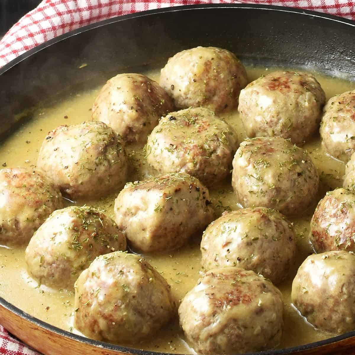 Side view of turkey meatballs in gravy in large shallow pan.