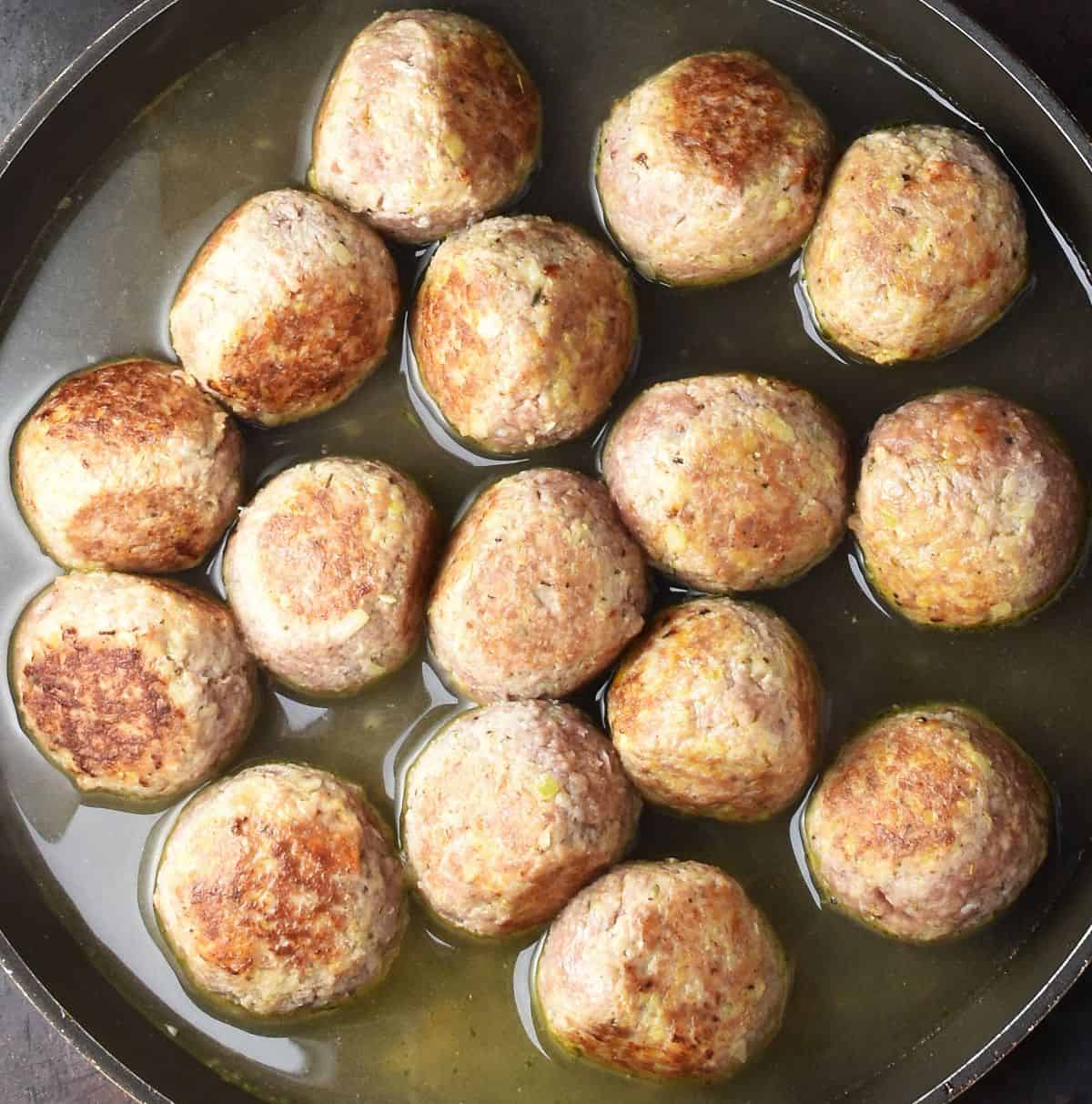 Browned meatballs with stock in large shallow pan.