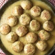 Top down view of turkey meatballs in gravy in large shallow pan.