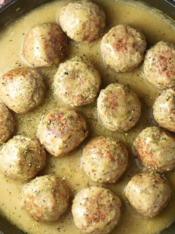 Top down view of turkey meatballs in gravy in large shallow pan.