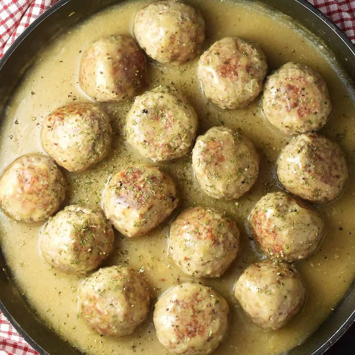 Top down view of turkey meatballs in gravy in large shallow pan.