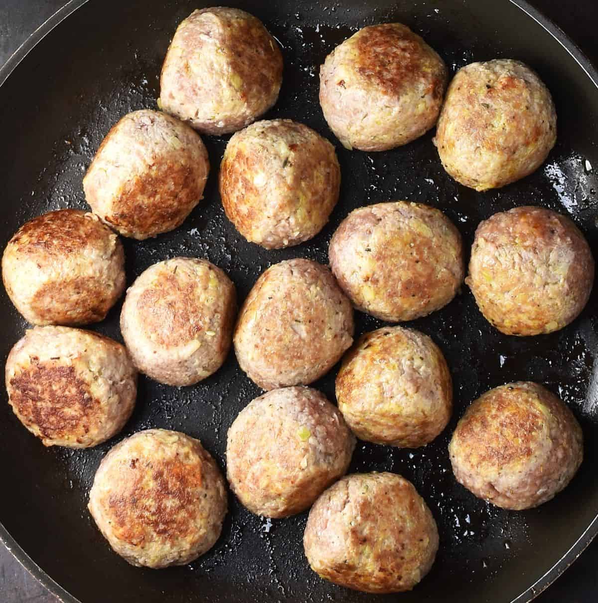 Top down view of browned turkey meatballs in large pan.