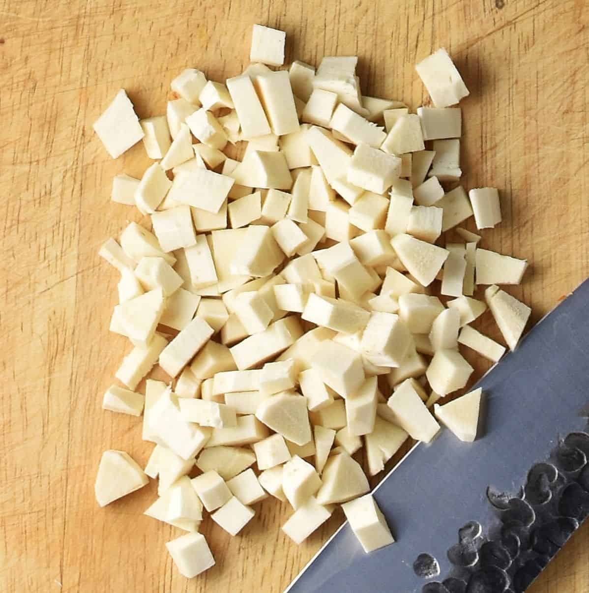 Peeled, finely chopped horseradish with knife on cutting board.