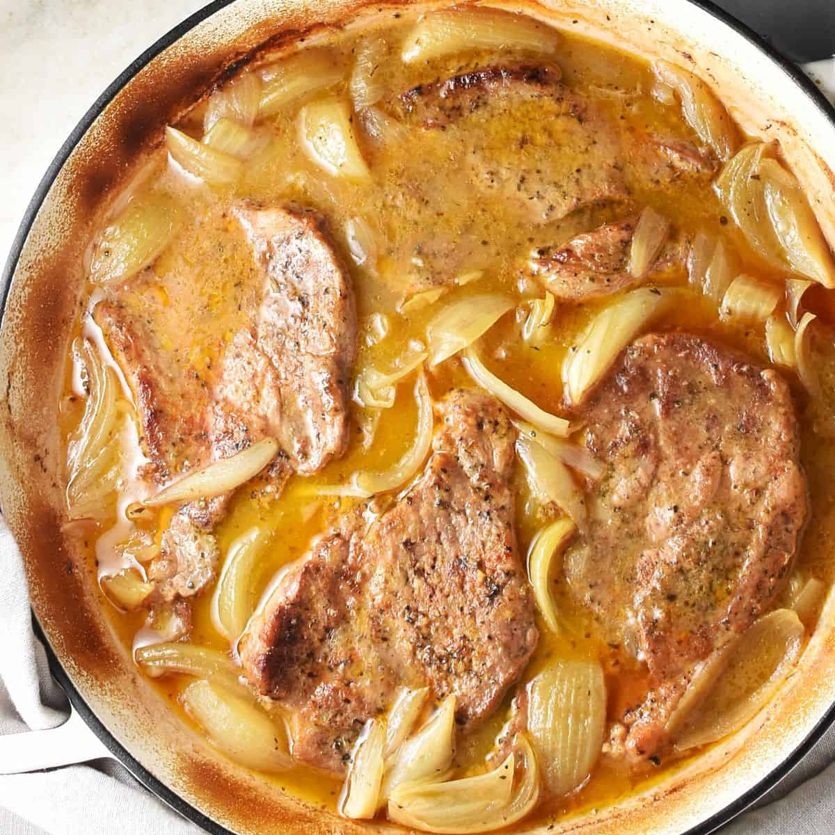 4 pork shoulder steaks braised with onion in large shallow pan.
