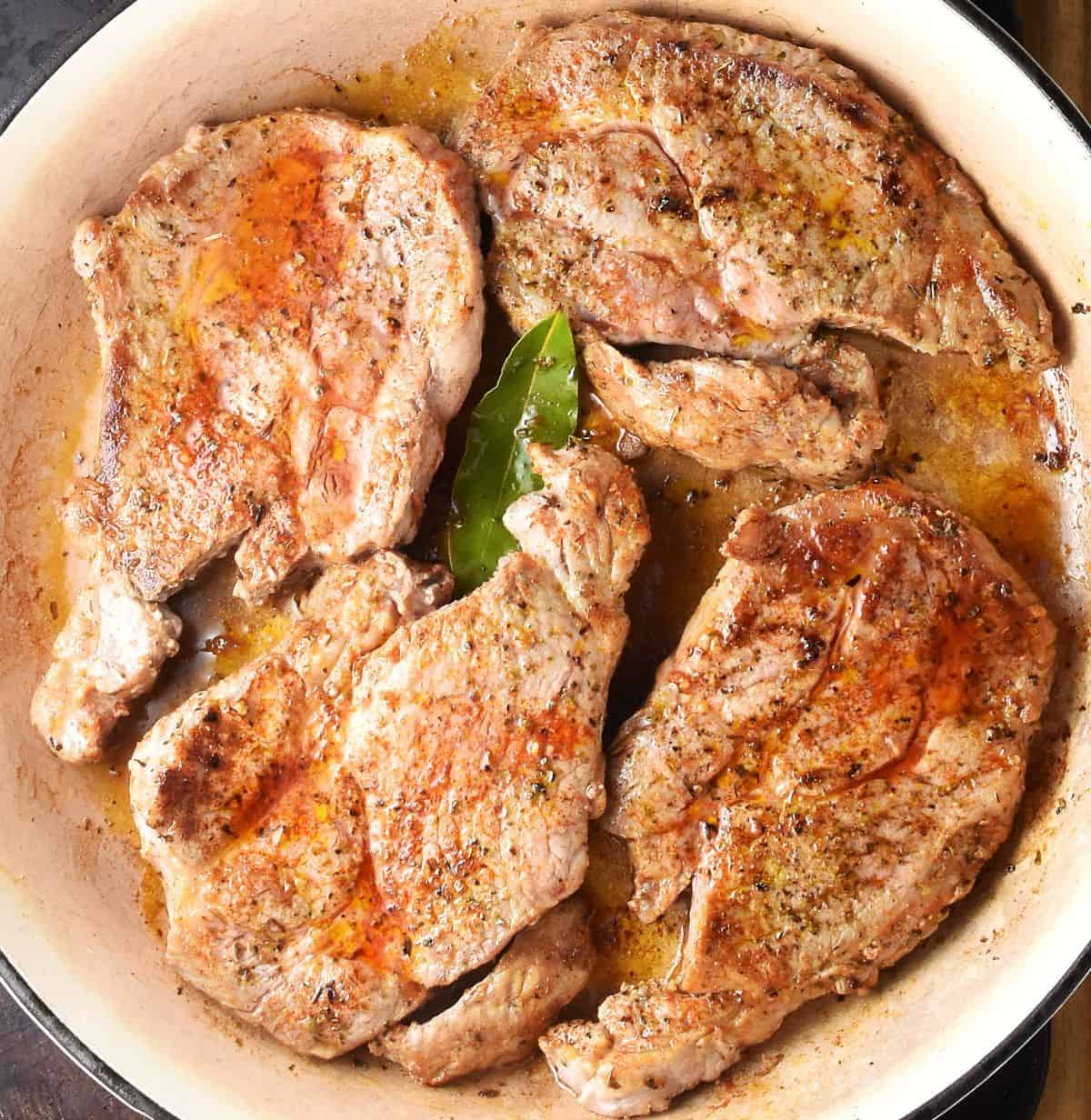 4 lightly browned pork steaks in shallow pan with bay leaf.